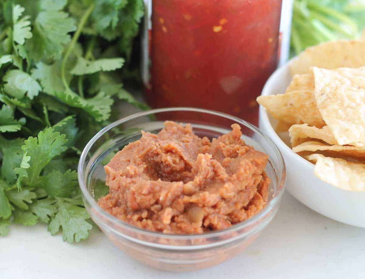 refried beans in abowl with fresh cilantro, bowl of tortilla chips and a jar of salsa