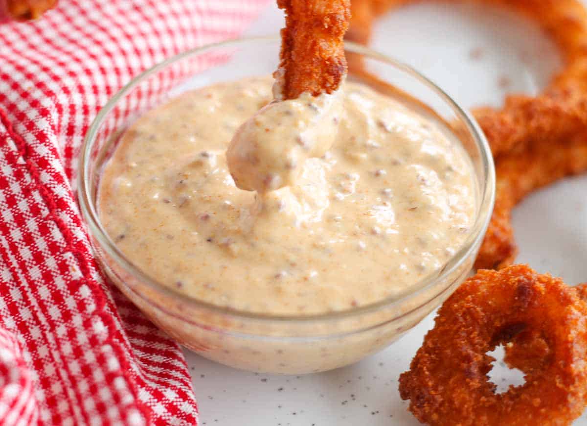 A baked onion ring being dipped into a dish of spicy dipping sauce