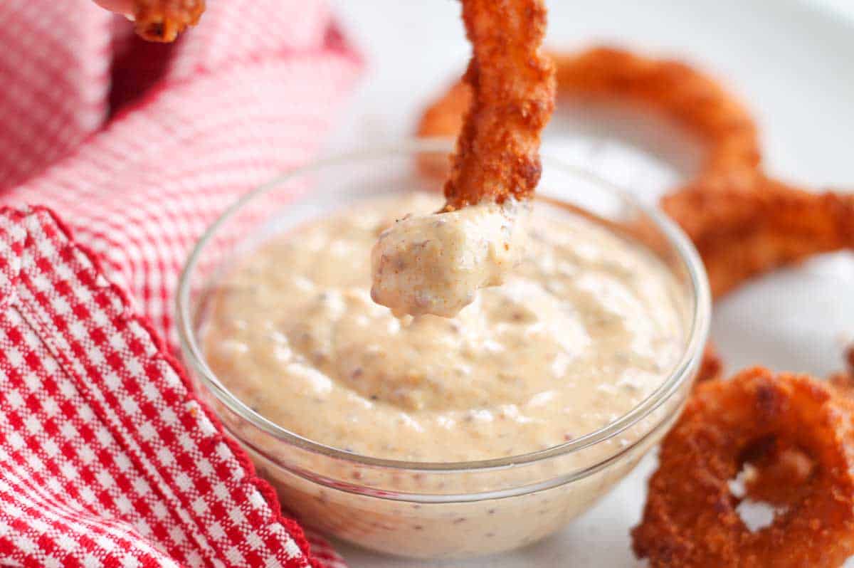 a baked onion ring being dipped into a dish of spicy dipping sauce