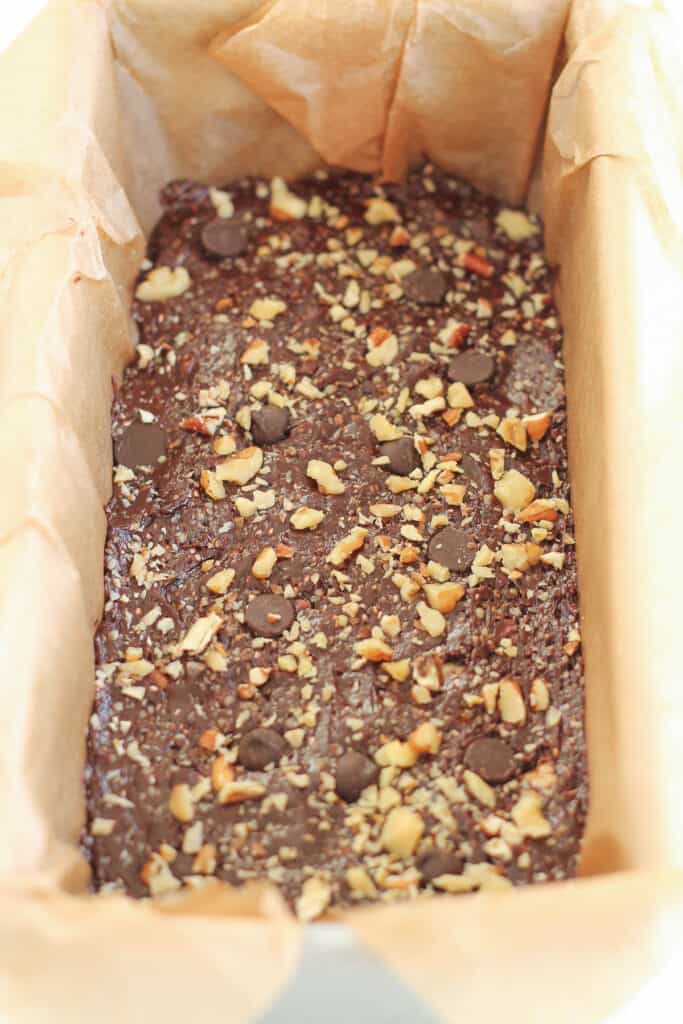 healthy chocolate mixture pressed into a parchment lined loaf pan with tosted nuts and dark chocolate chips on top