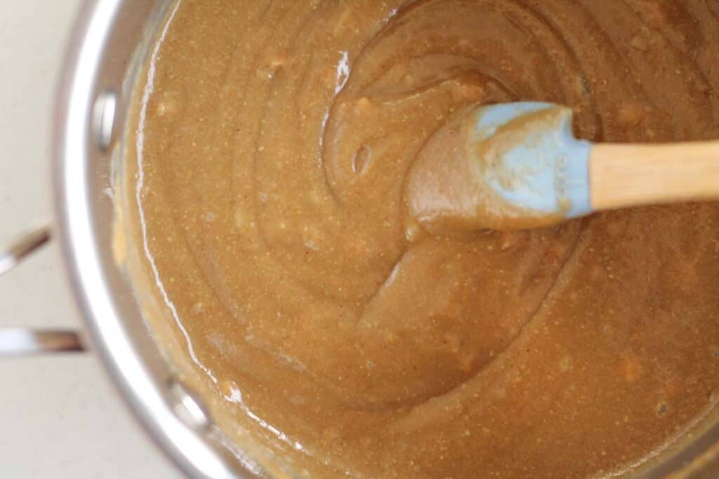 sunflower seed butter and peanut butter being stirred in a saucepan by a spatula
