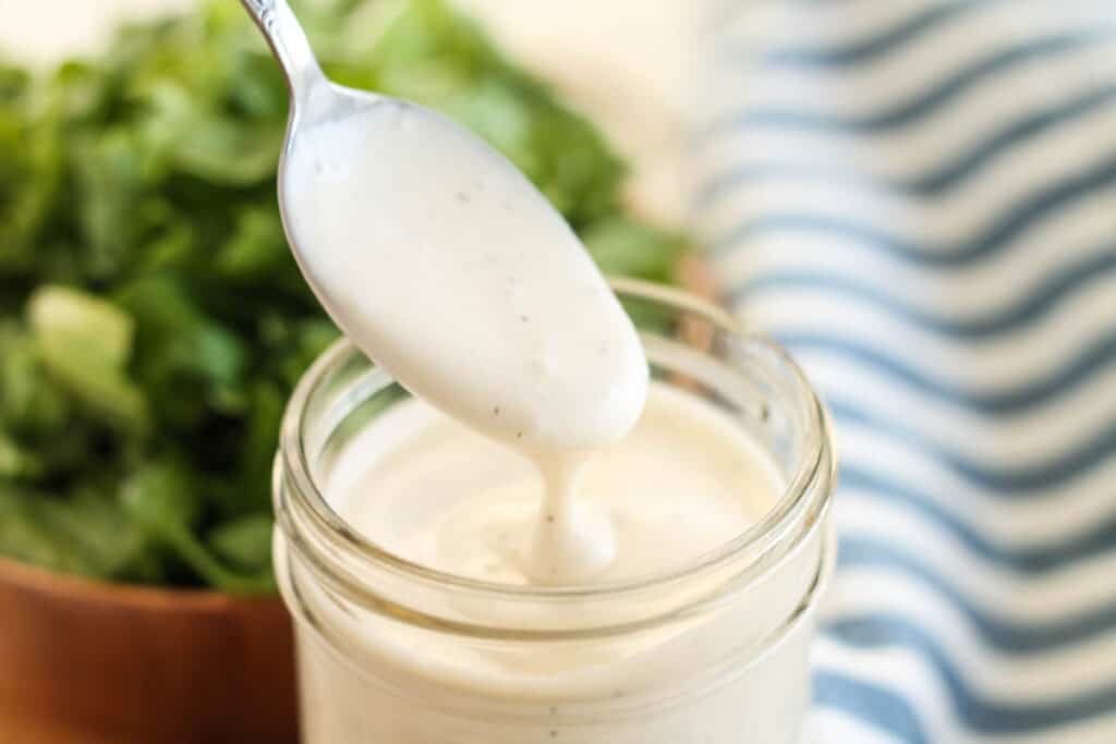homemade ranch dressing in a jar with a spoon being dipped into it