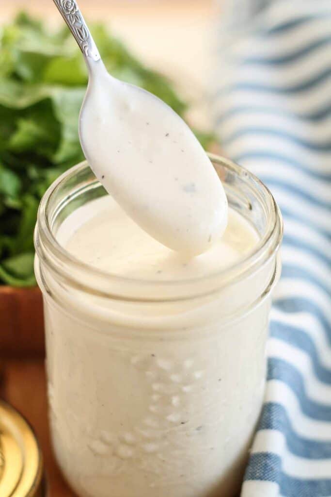 homemade ranch dressing in a jar with a spoon being dipped into it