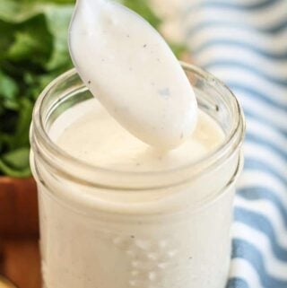 homemade ranch dressing in a jar with a spoon being dipped into it
