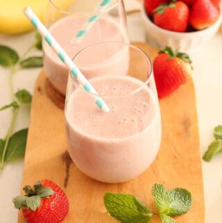 vegan strawberry banana smoothie in a glass with a blue striped straw