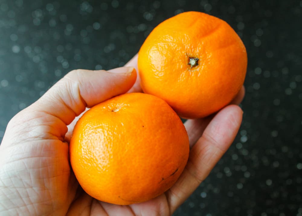a hand holding 2 oranges.