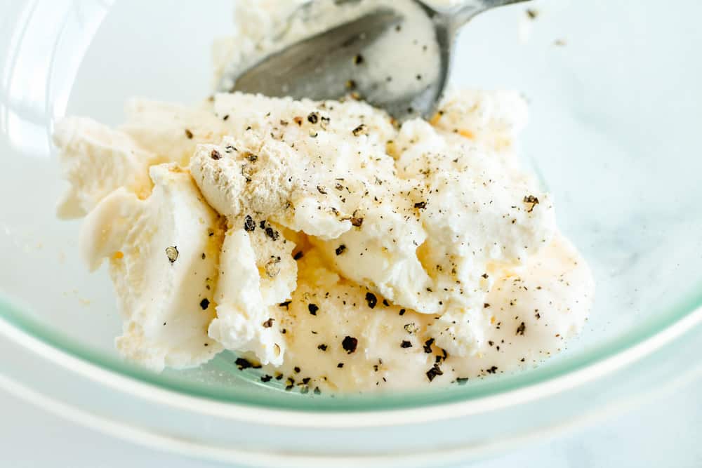 a bowl of cream cheese being stirred with salt and pepper.