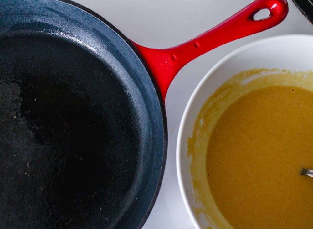 a cast iron pan next to a bowl of batter.