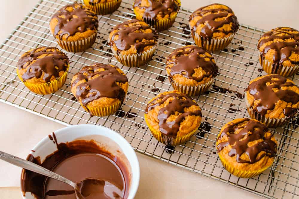 chocolate being drizzled on top of baked cupcakes.