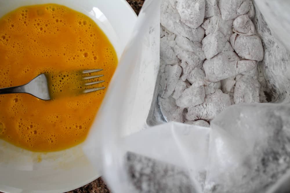 a breading station set up with a bowl of beaten eggs and a bag of chicken pieces being dredged in arrowroot starch.