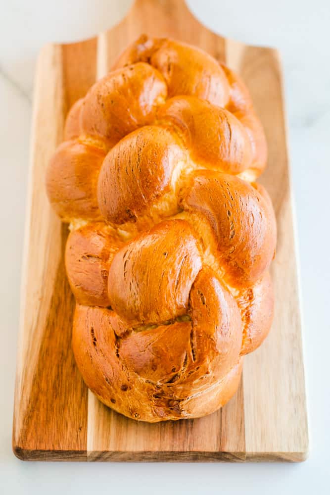 a loaf of braided challah bread on a wooden board.