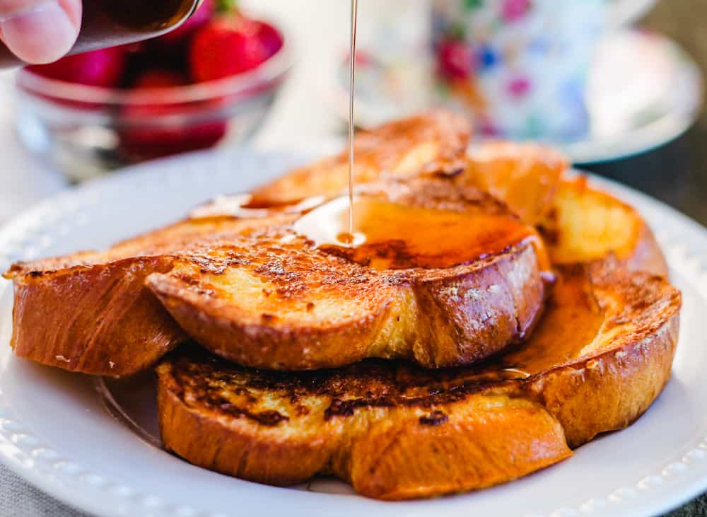 challah french toast on a plate being drizzled with maple syrup.