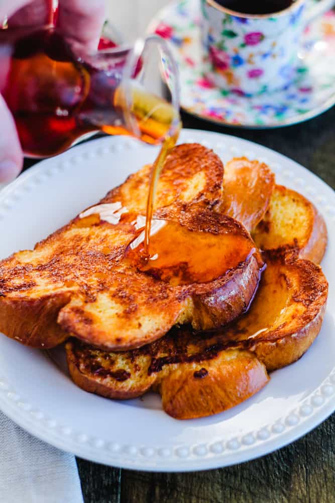 challah french toast on a plate being drizzled with maple syrup.