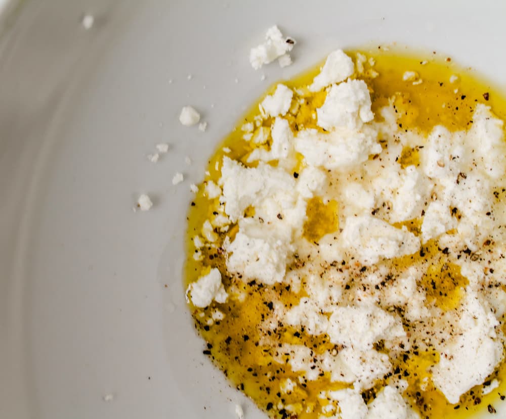 a mixing bowl with olive oil, seasonings and a clump of soft cheese.