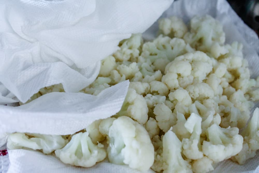 cooked cauliflower florets being patted dry with a paper towel.