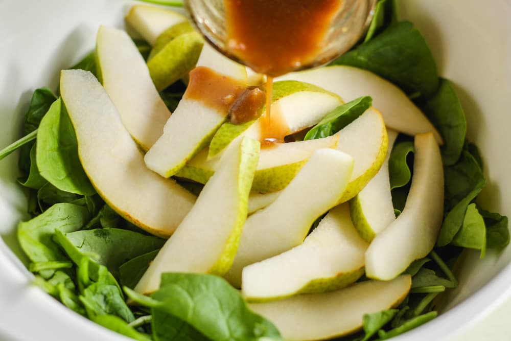 balsamic dressing being poured over pears and spinach.