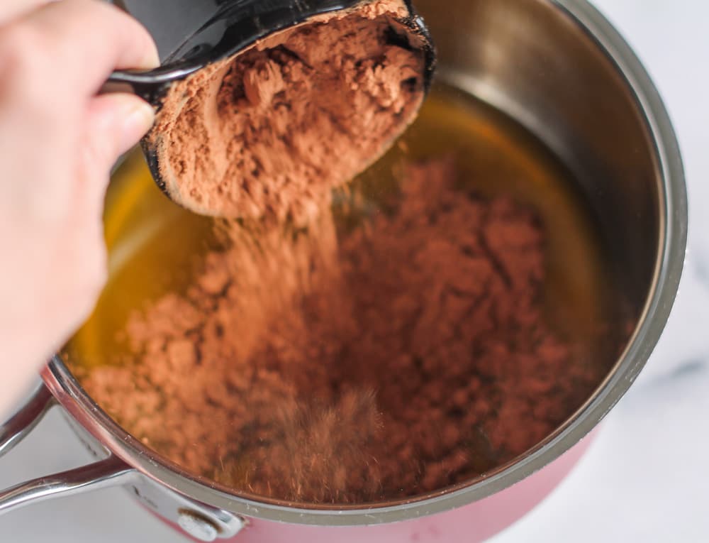 cacao powder being dumped into a saucepan.