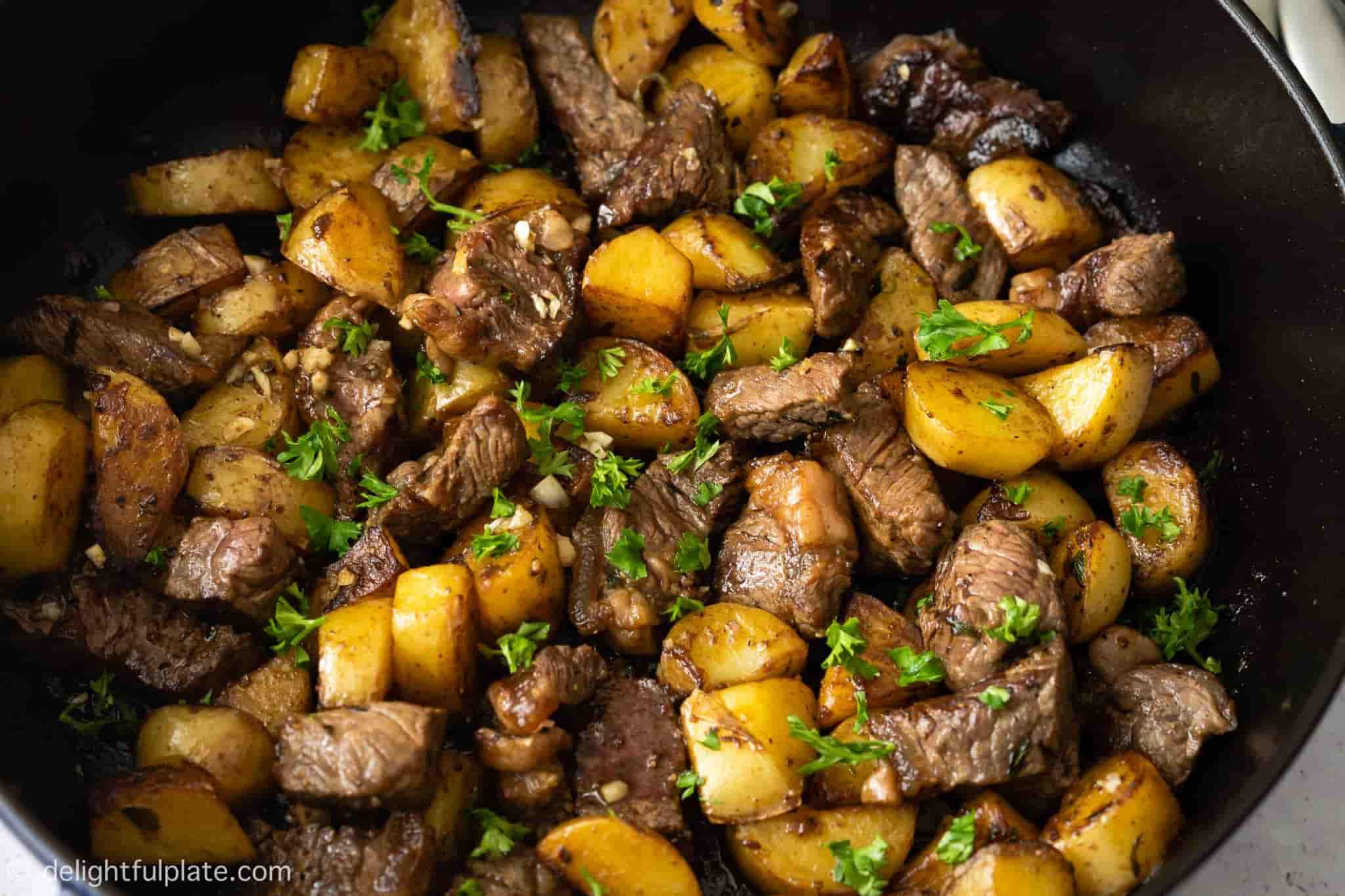 steak bites and potatoes in a pan.