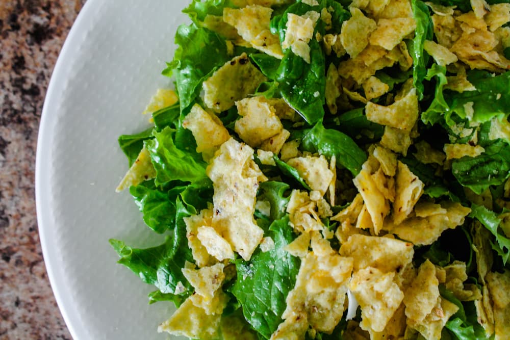 tortilla chips crumbled over a plate of lettuce.