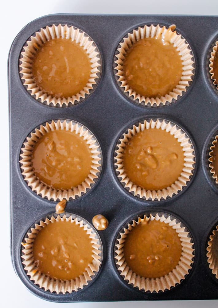 a muffin tin lined with parchment paper cups and filled with sun butter cups ingredients.