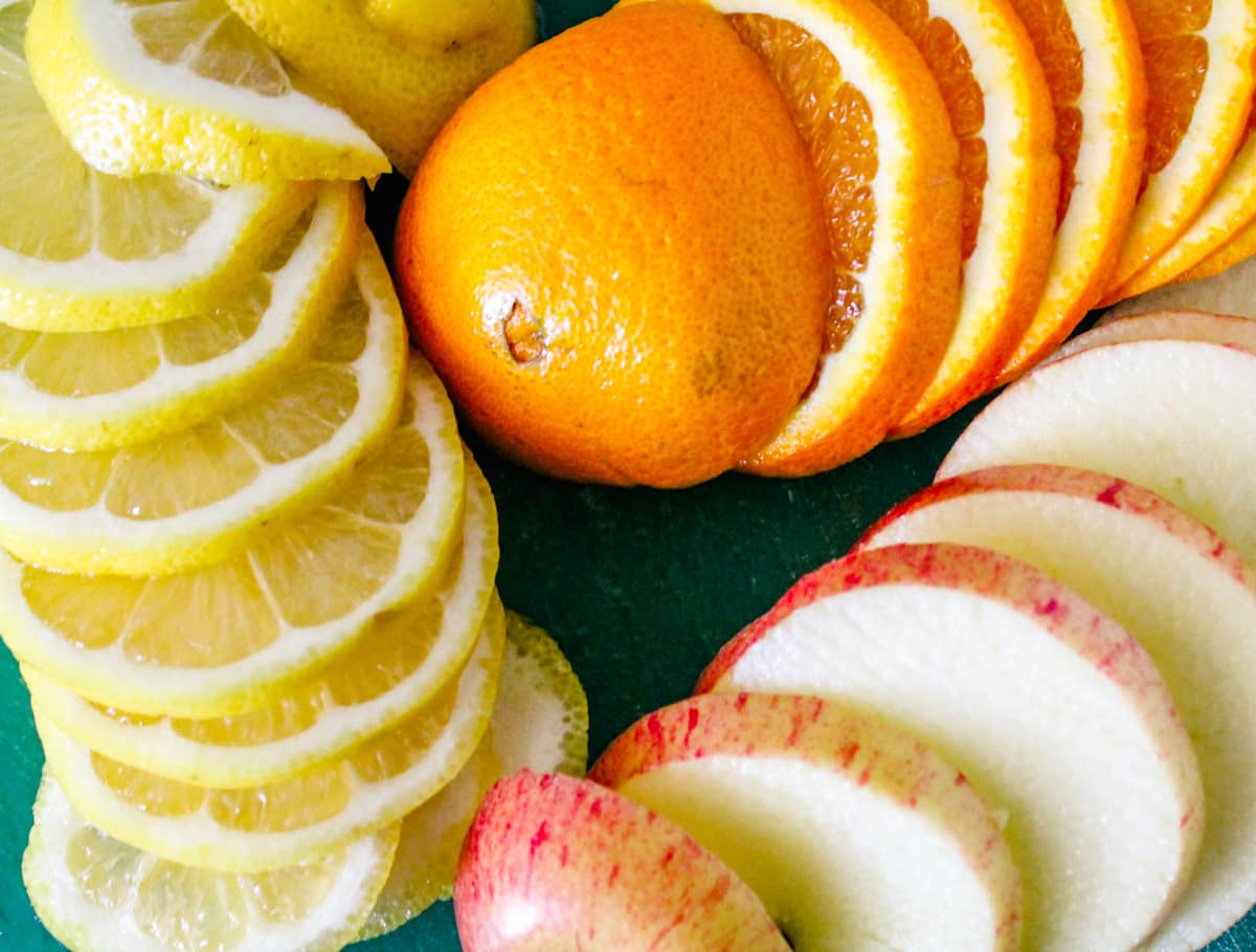 sliced lemons, sliced oranges, and apple slices on a cutting board.