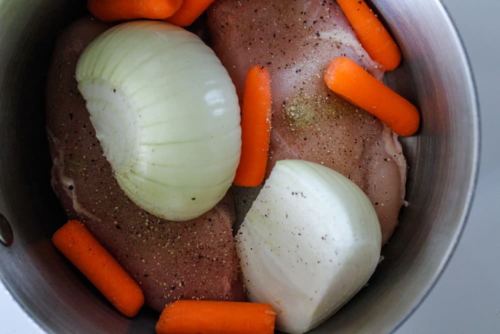 chicken in a pot with carrots and onion.