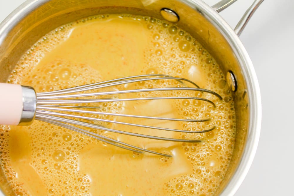 a saucepan or golden liquid being whisked with a whisk.