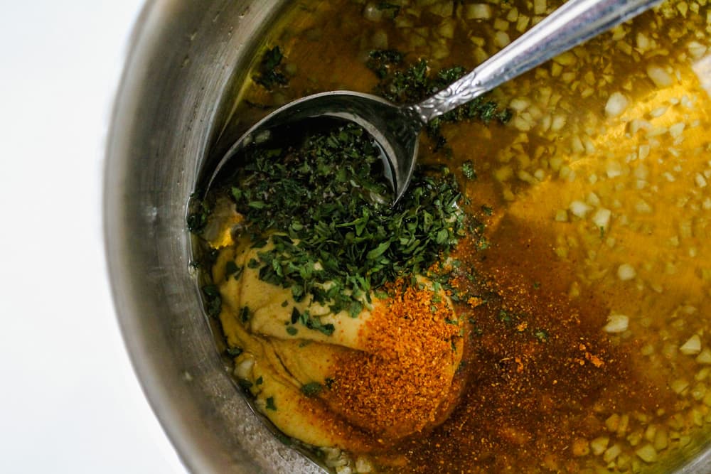 dijon mustard and other spices being stirred into a garlic and olive oil.