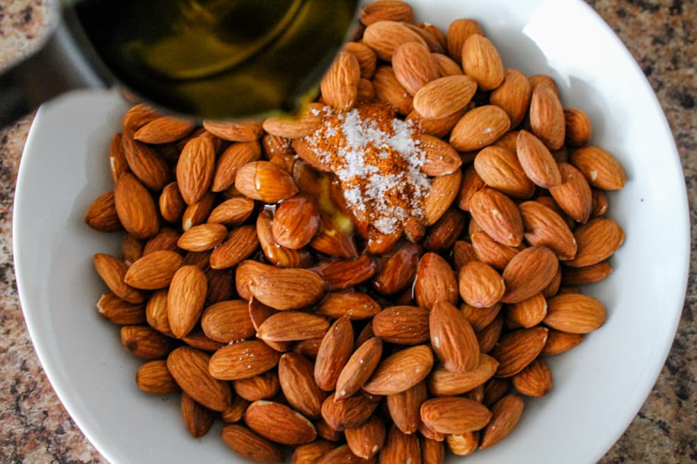 olive oil being poured over a bowl of almonds.