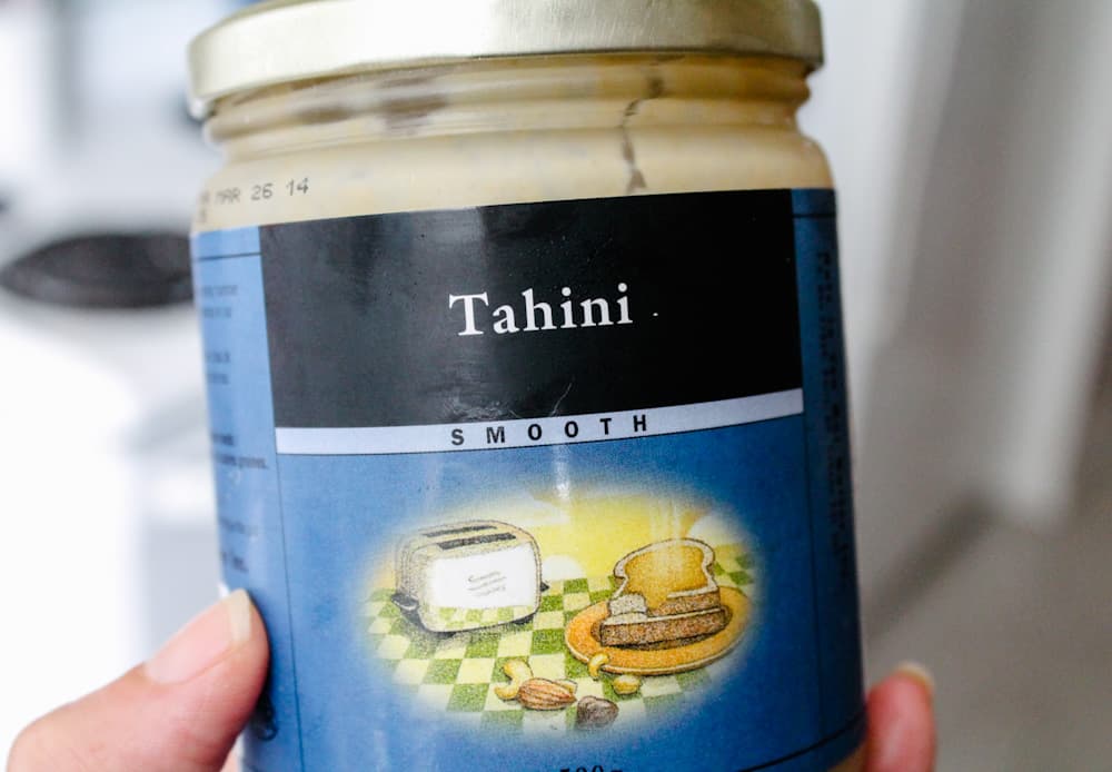 a hand holding a jar of tahini.