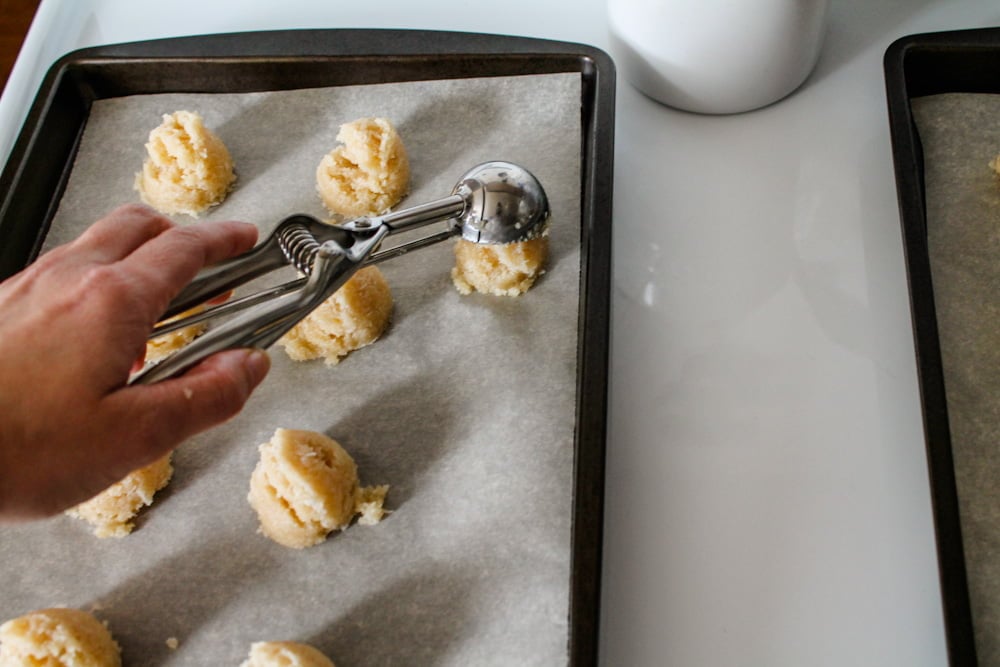 a hand scooping macaroon dough onto a baking sheet.
