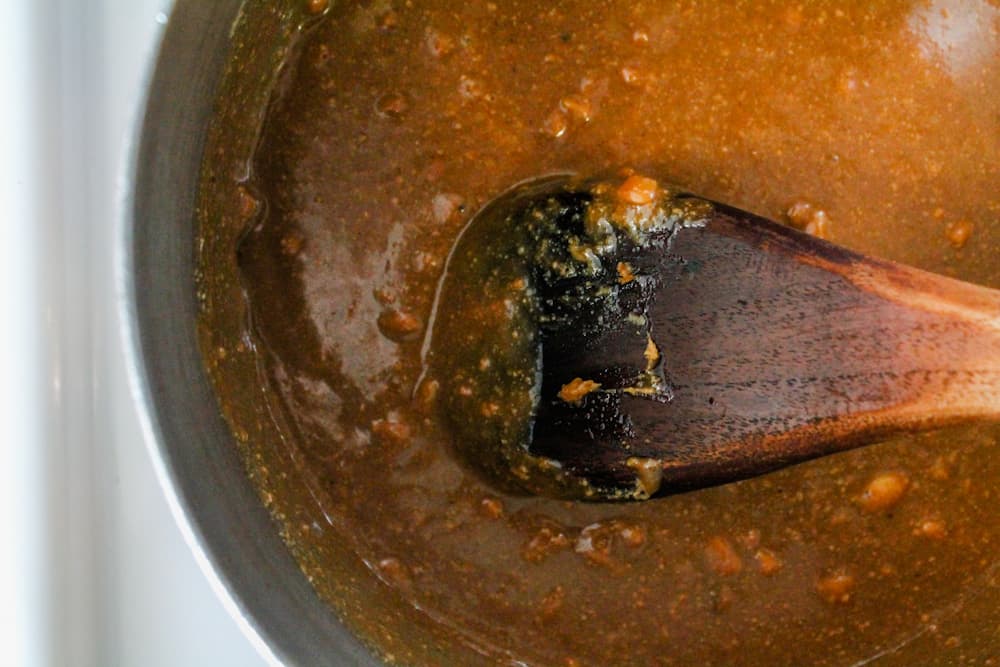 a wooden spoon stirring ingredients in a saucepan.