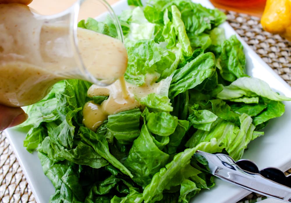 dijon dressing being poured over a plate of greens.