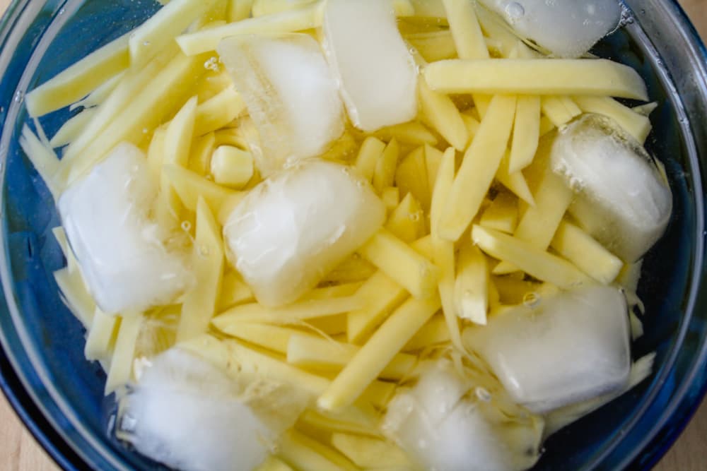 a bowl of sliced potatoes soaking in ice water.