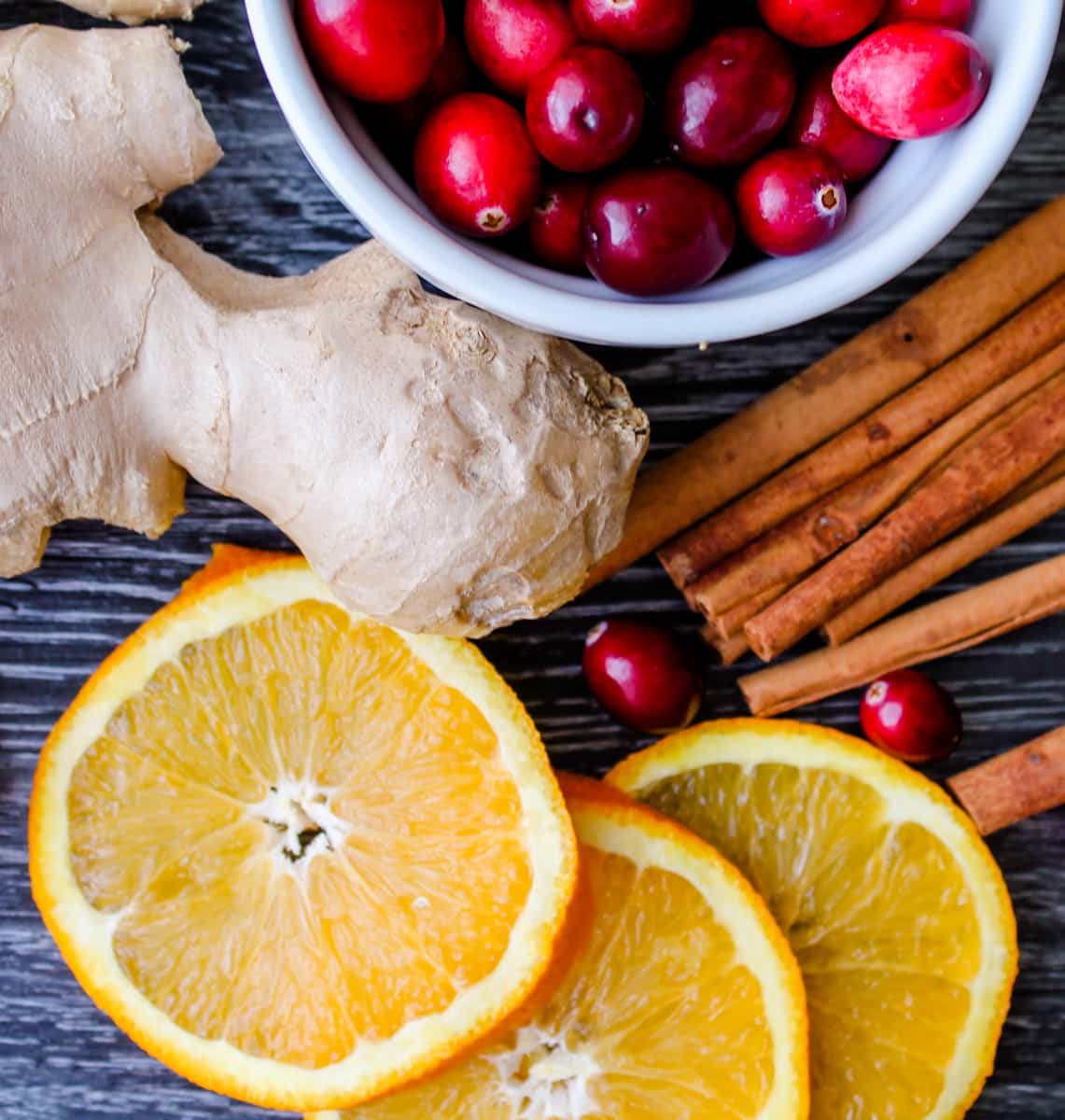 ginger, orange slices, cranberries and cinnamon sticks on a counter.
