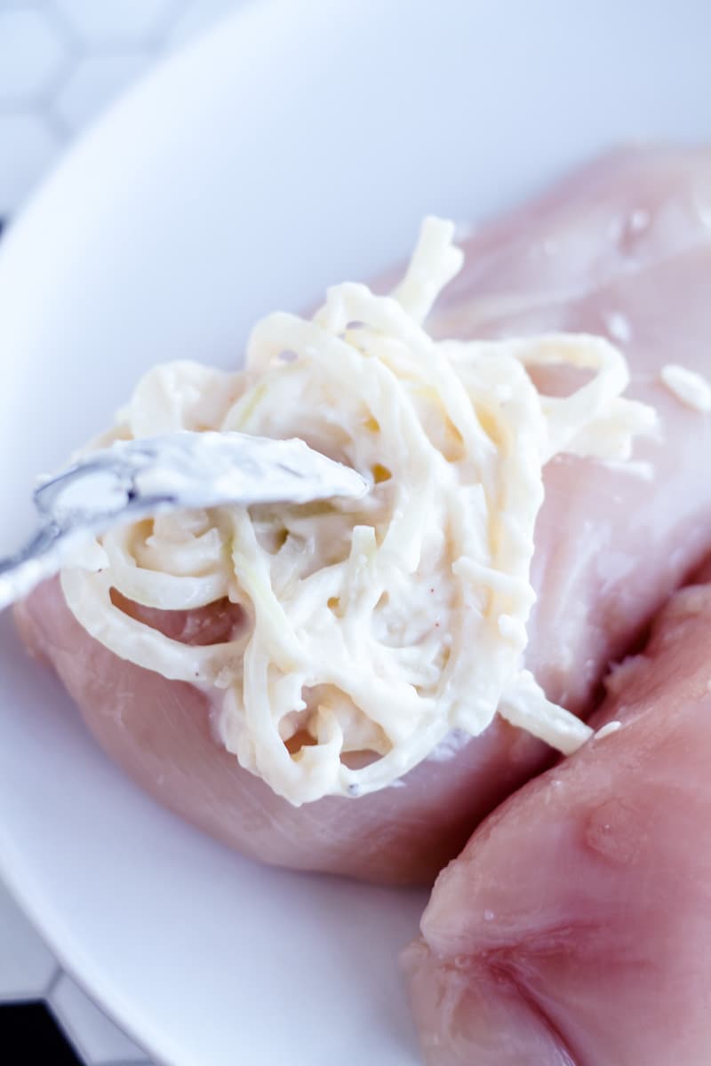 a dollop of parmesan mayo mixture being spread onto a chicken breast.