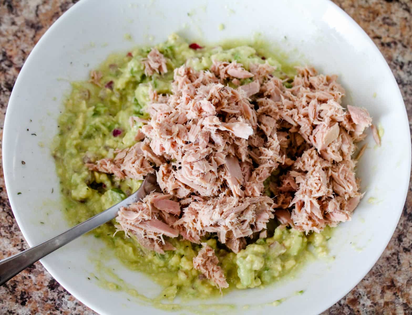 tuna on top of mashed avocado in a bowl.