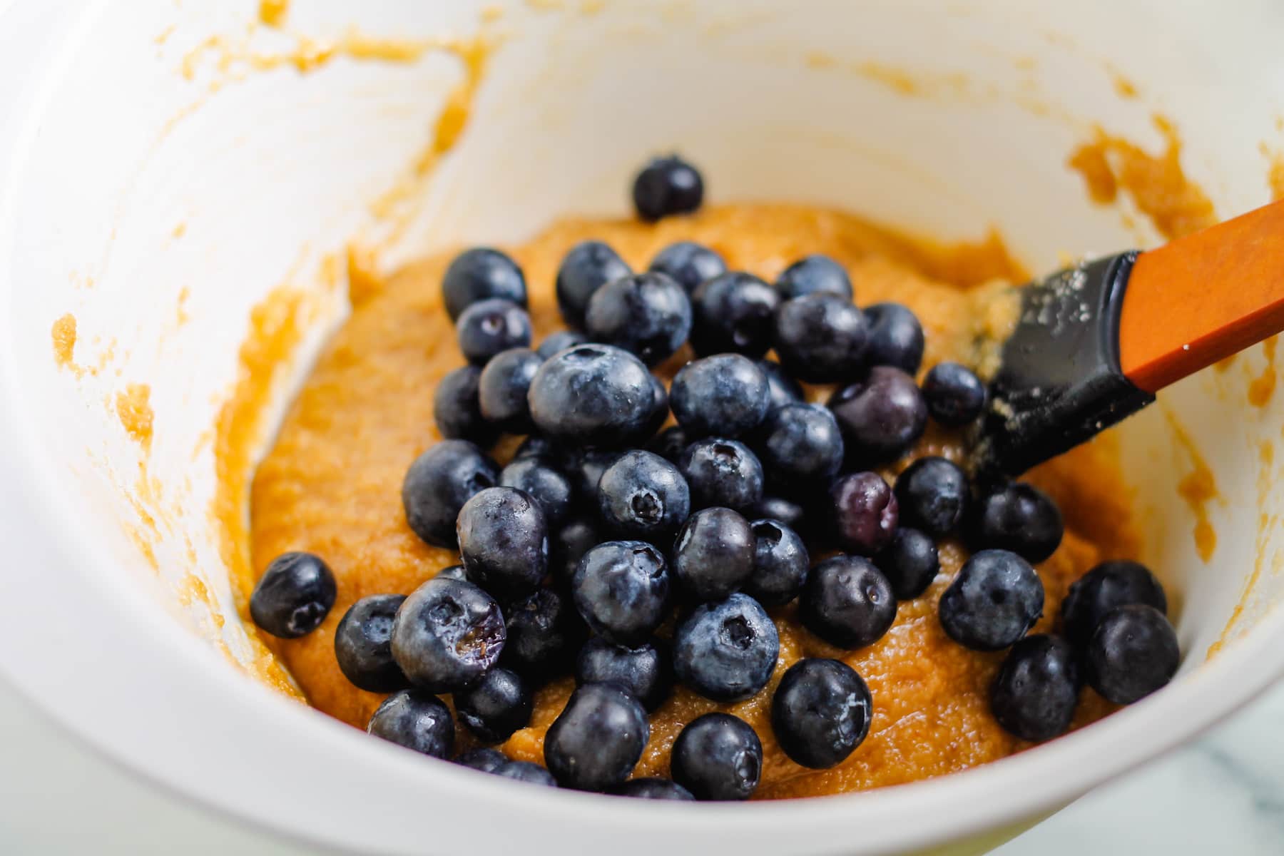 blueberries being folded into batter in a mixing bowl.