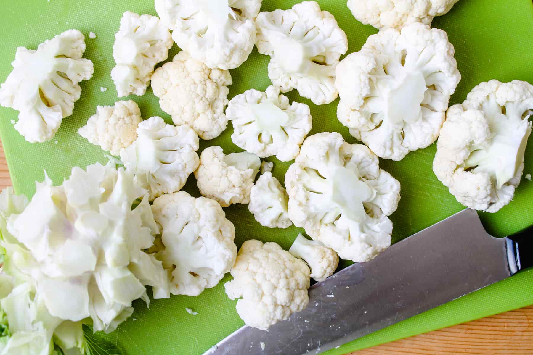 cauliflower florets being chopped on a cutting board.