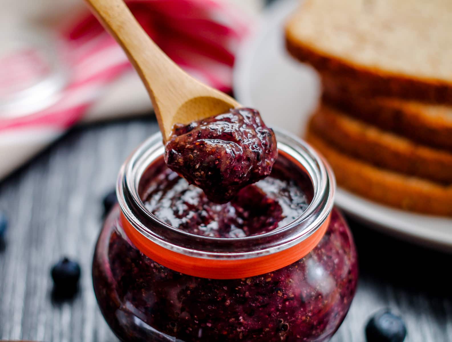 a spoon scooping healthy blueberry chia jam from a jar.