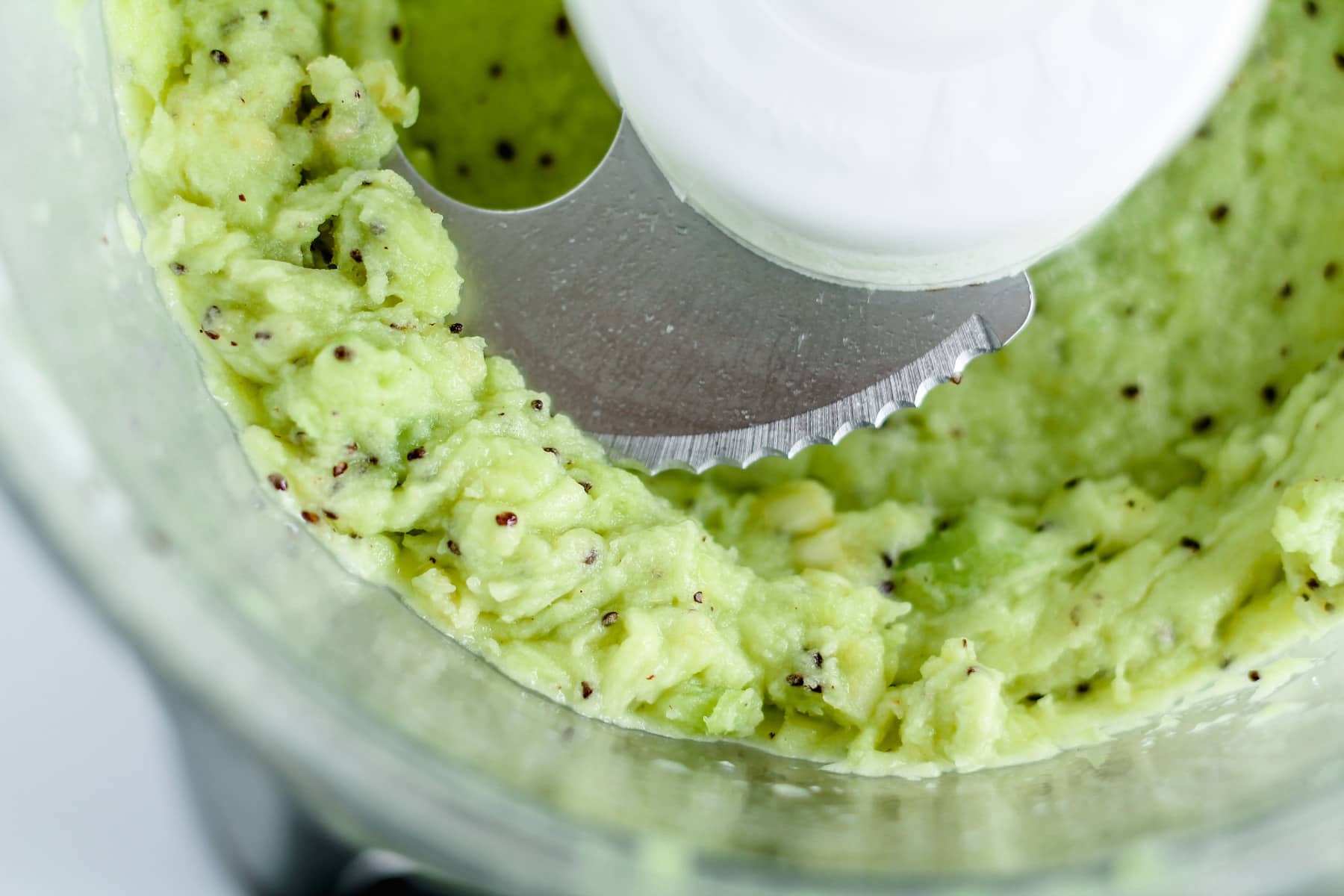 frozen kiwi chunks being blended in a food processor.