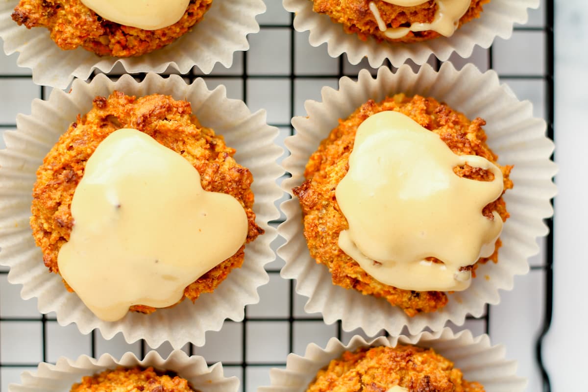 frosted carrot muffins cooling on a wire rack.