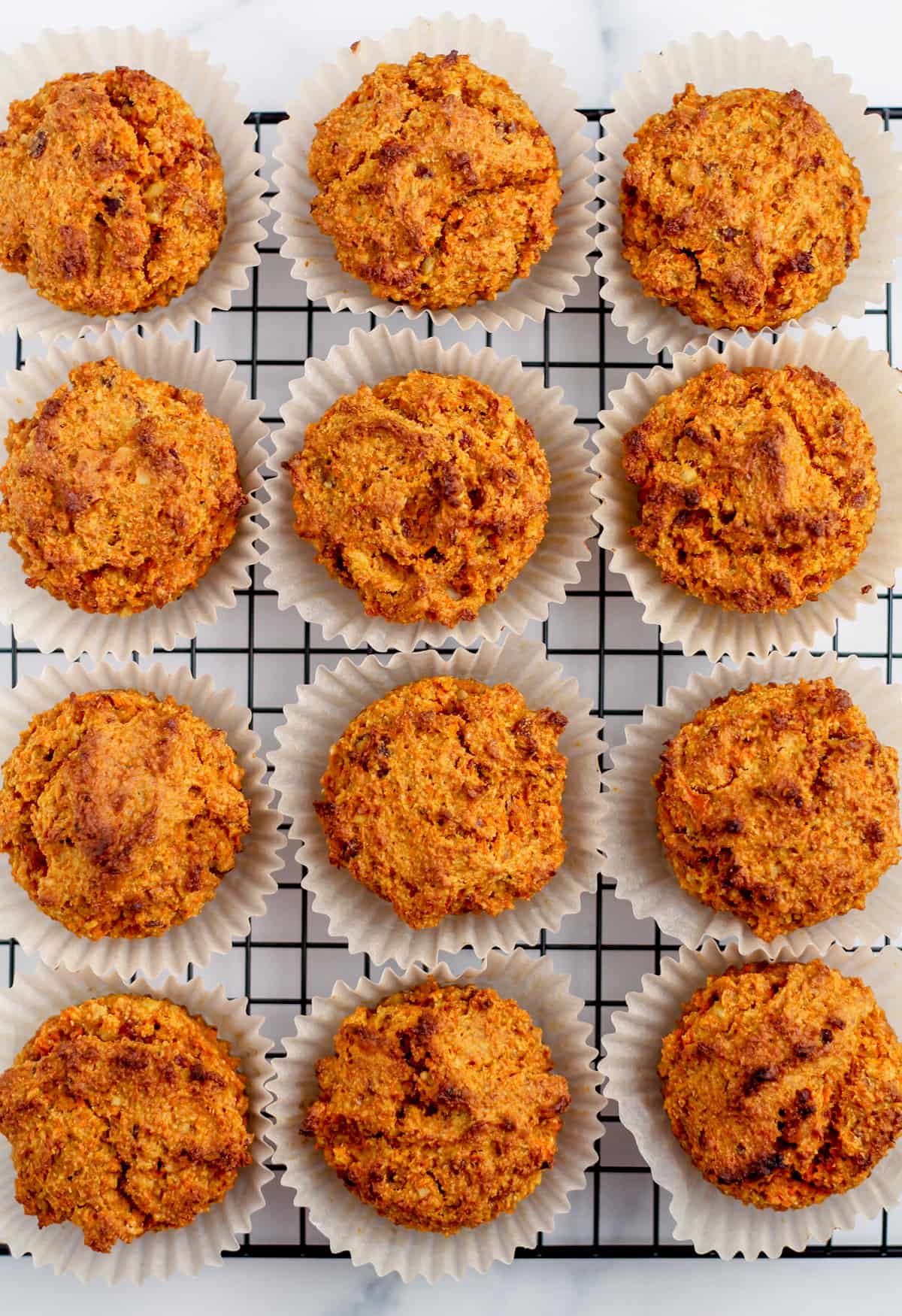 a wire rack with freshly baked carrot spelt flour muffins.