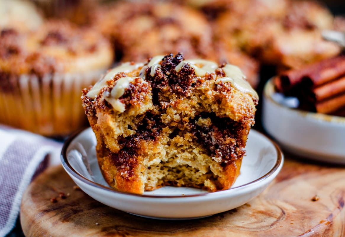 an almond flour cinnamon roll muffin on a plate with a bite out of it.