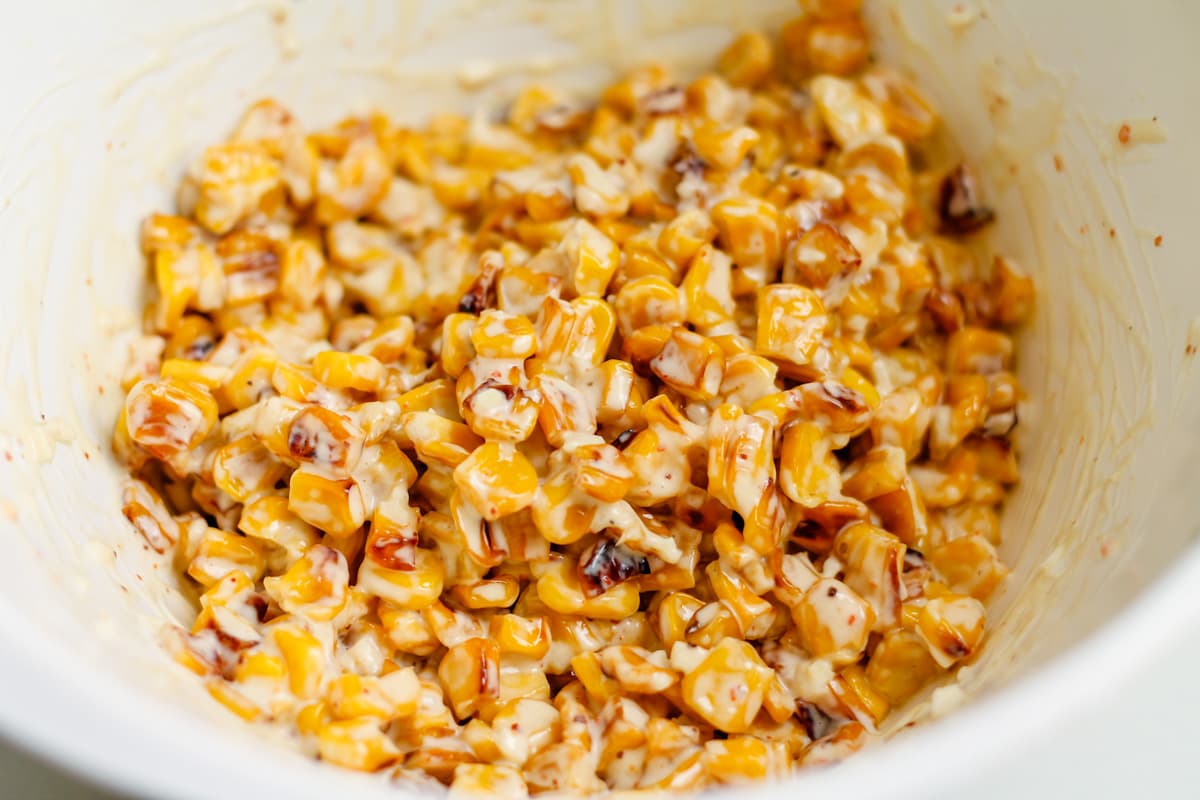 dressing tossed in with charred corn in a mixing bowl.