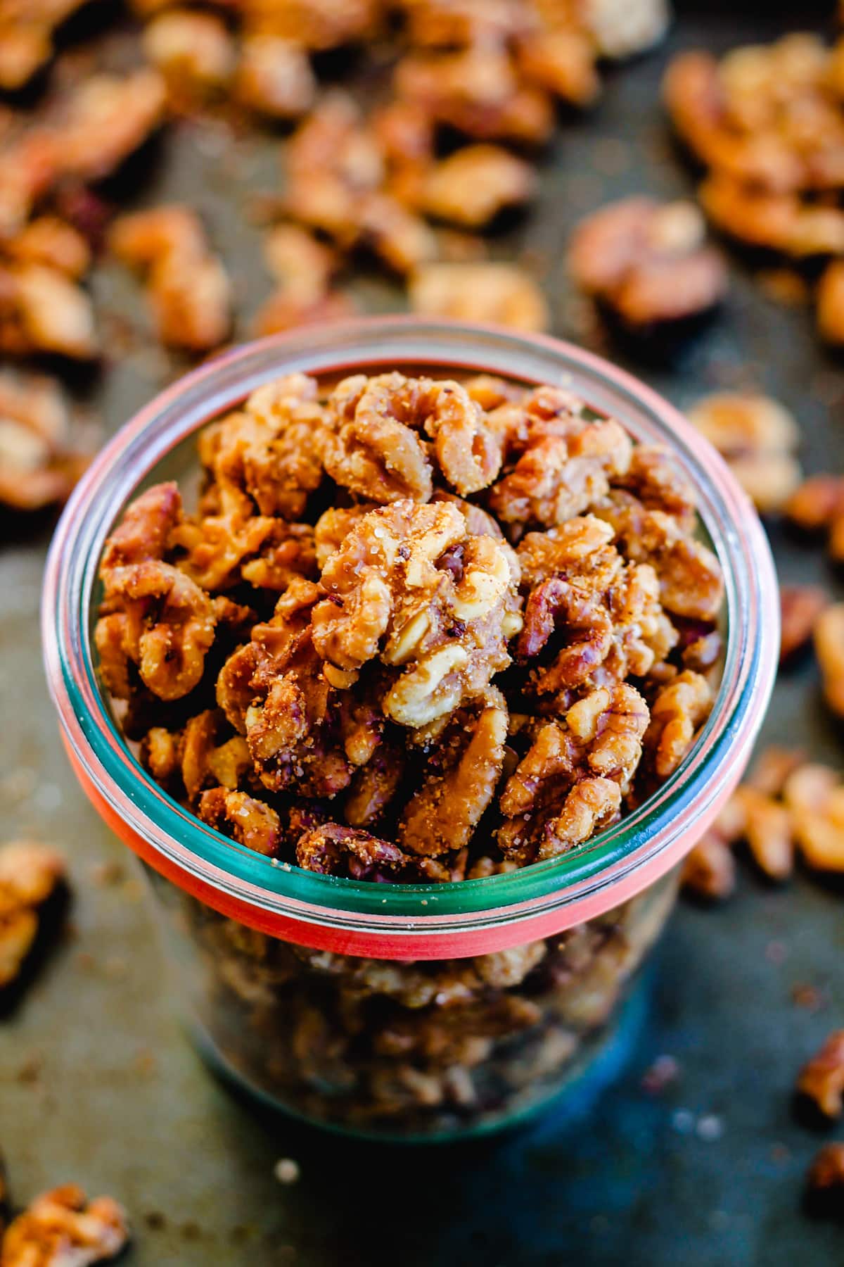 a glass jar of spiced walnuts on a baking sheet.