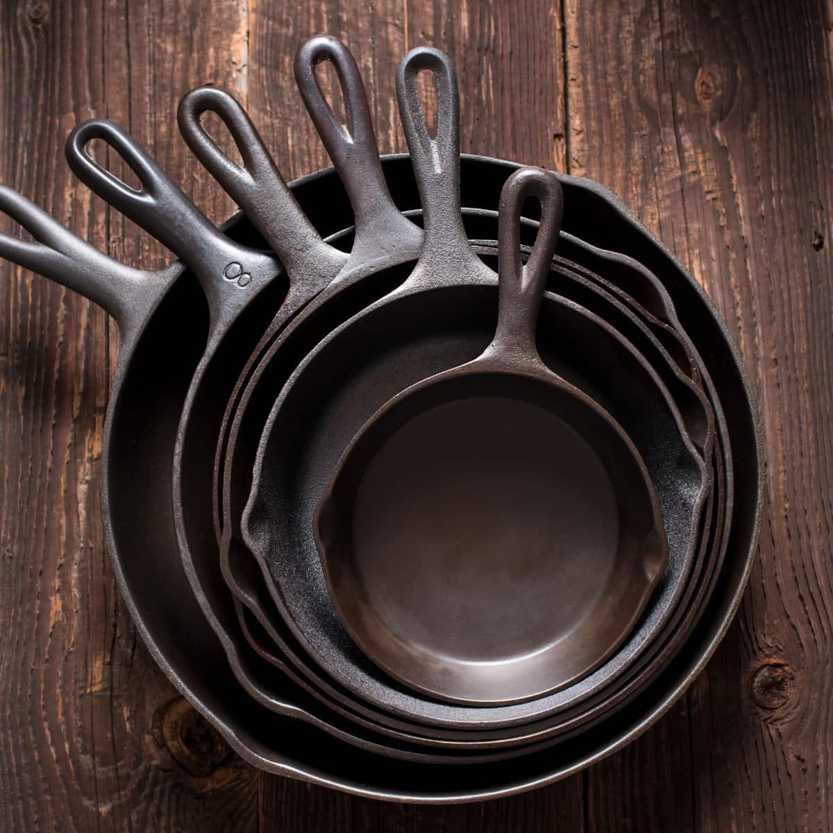 A pile of cast iron skillets on a wooden table.
