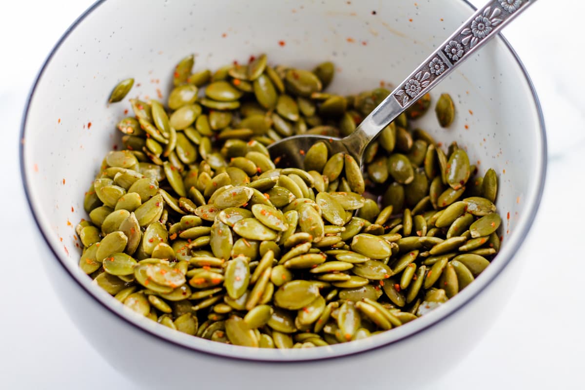 A mixing bowl with a spoon mixing the pumpkin seeds.