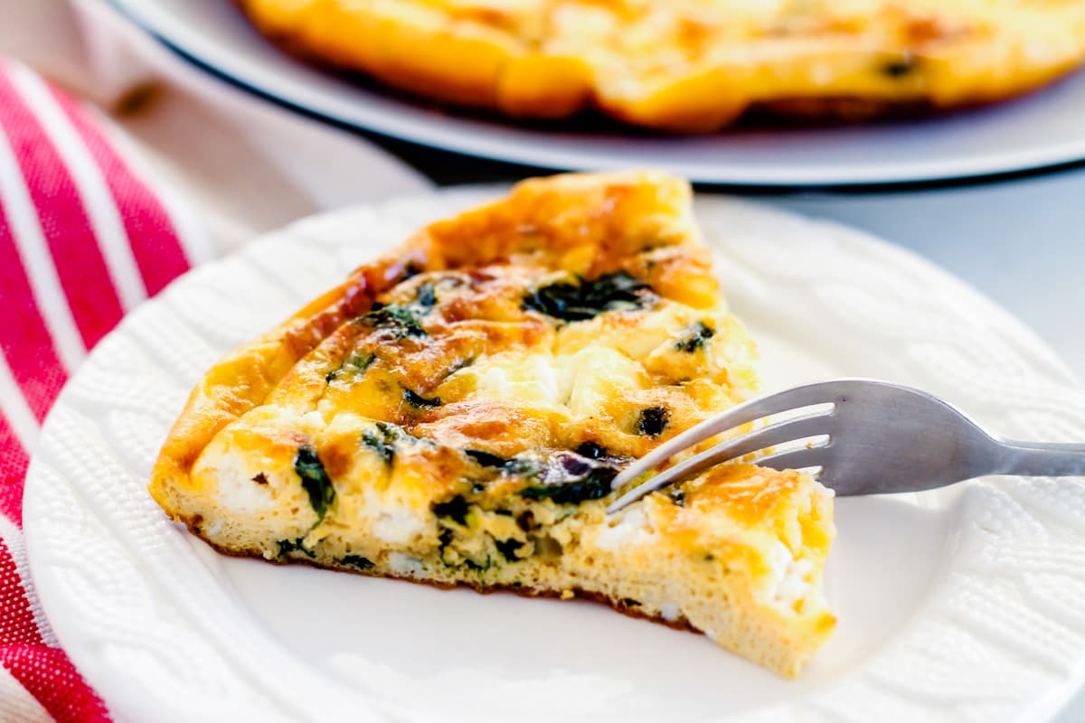 a fork cutting into a wedge of goat cheese frittata.