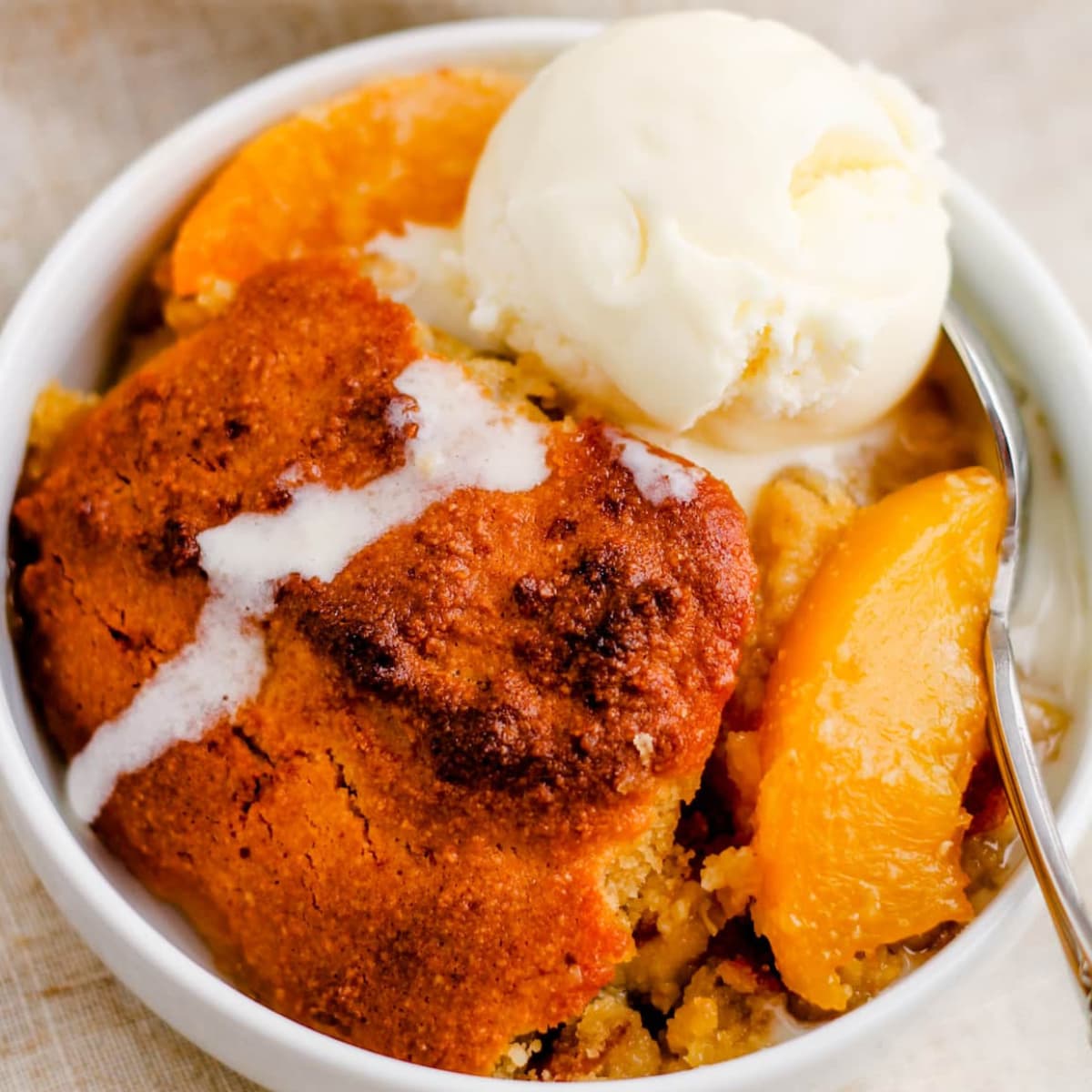 a bowl of peach cobbler with a scoop of ice cream on top.